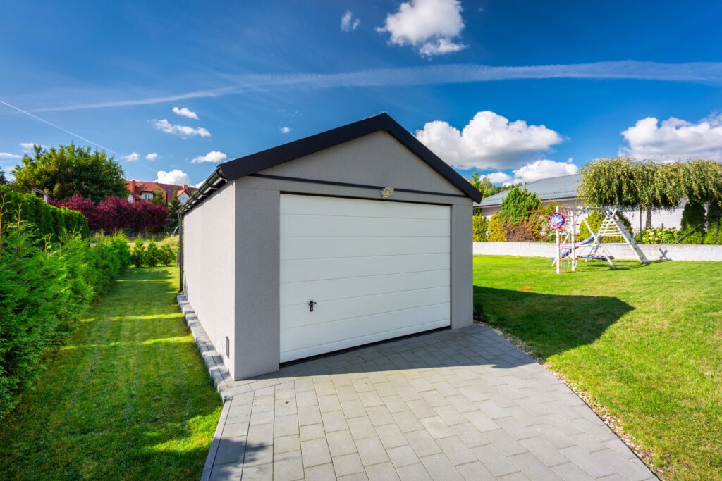 TM Exterior Solutions LLC installing white sectional garage door on detached backyard garage with paver driveway and lawn